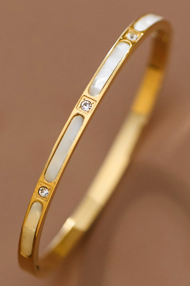 Gold bracelet with white stones on a brown background
