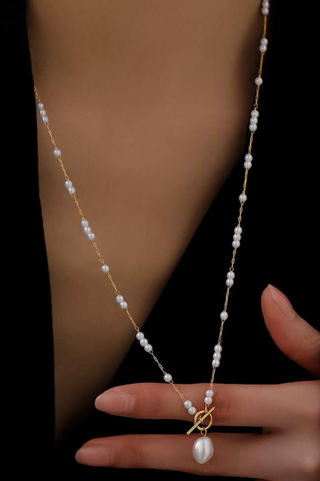 Pearl necklace with a pendant held by a hand against a dark background