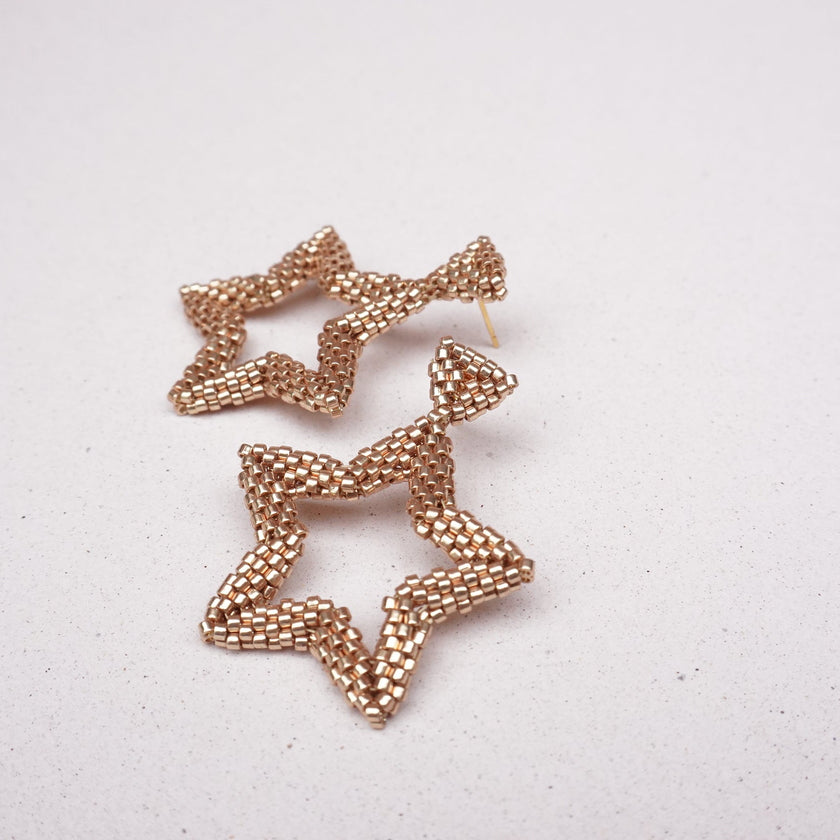 Champagne star-shaped earrings on a light gray background