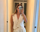Woman taking a mirror selfie wearing a white outfit with a vest and lace shorts.