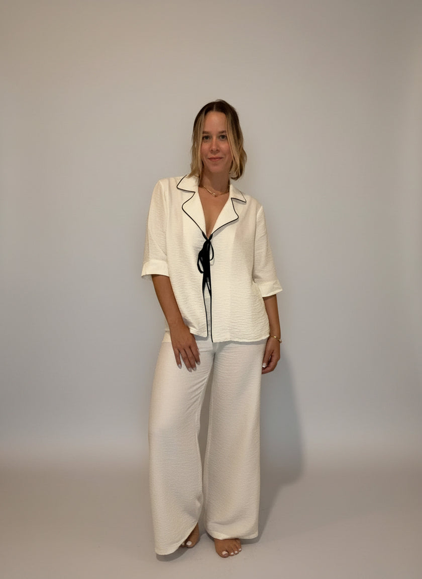 Woman in a white outfit standing in front of a wall with framed pictures.
