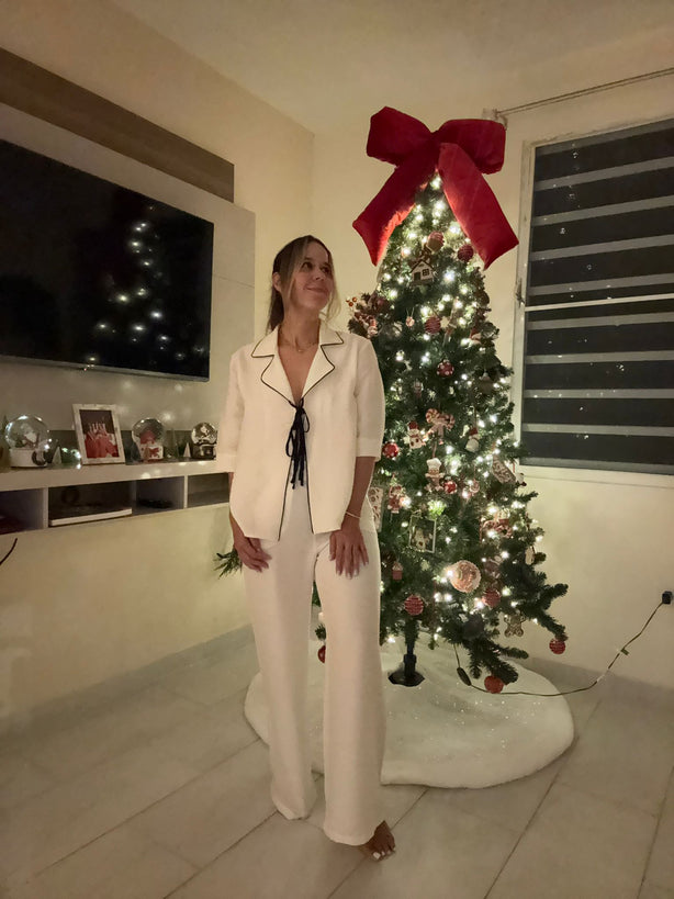 Woman standing in a living room with a decorated Christmas tree and large red bow.