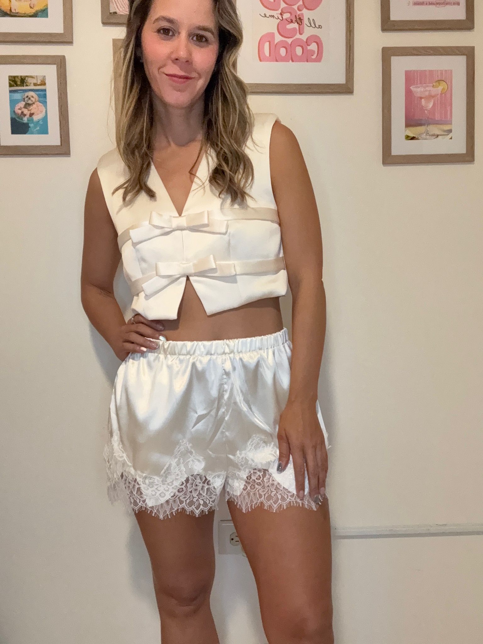 Woman wearing a white outfit with lace details against a wall with framed pictures.
