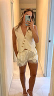 Woman taking a mirror selfie wearing a white lace nightgown with a cream-colored vest.