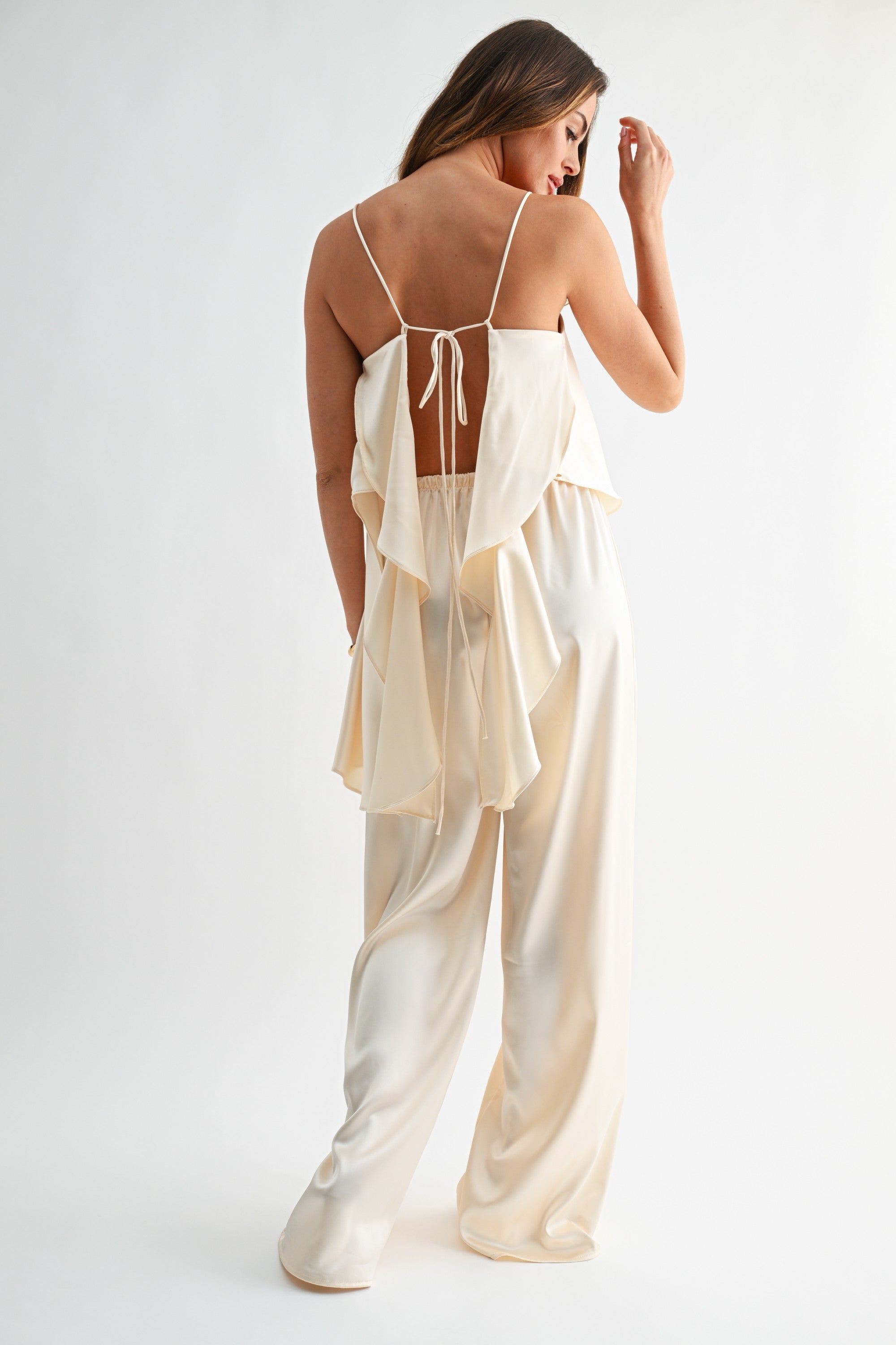 Woman wearing a light-colored outfit with a sheer top and wide-leg pants on a white background